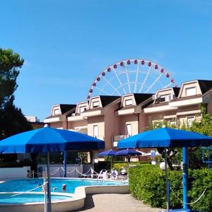 ein Riesenrad und ein Pool mit blauen Sonnenschirmen in der Unterkunft B&C Apartments LA POSTA Home in Lido di Jesolo