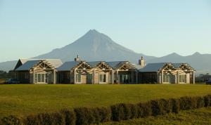 a house on a field with a mountain in the background at Taranaki Country Lodge in New Plymouth