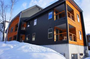 a black building with snow in front of it at Big Bear Chalets & Apartments in Hakuba