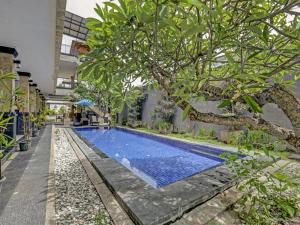 a swimming pool with a tree next to a building at Super OYO 3904 Kiki Residence Bali in Seminyak