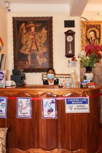 Una mujer con una máscara detrás de un mostrador con señales en Fuente de Agua Hotel, en Cusco