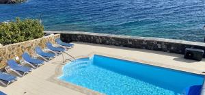 a swimming pool next to chairs and the ocean at Seafront Puerto Calero Villa in Puerto Calero