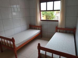two beds in a small room with a window at Residencia Siqueira in Garopaba