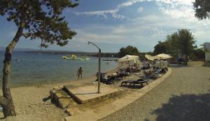 a group of people sitting on a beach with a boat in the water at Apartmani Zaric in Malinska