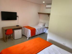 a room with two beds and a desk and a tv at Pousada Brisas do Vale in Vale do Capao