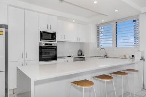a white kitchen with a large white counter and stools at Golden Sands on the Beach - Absolute Beachfront Apartments in Gold Coast