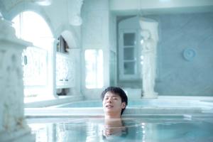 Um homem está a nadar numa banheira. em Shinjuku Kuyakusho-mae Capsule Hotel em Tóquio