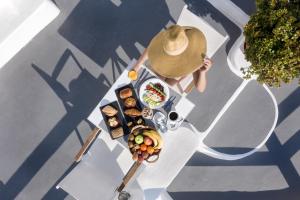 a person in a hat sitting at a table with food at Caldera Premium Villas in Oia