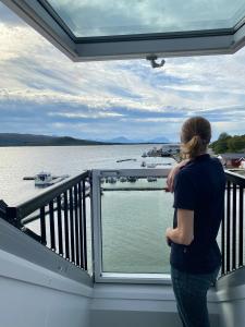 Una mujer parada en un balcón con vistas al agua en Senja Fjordhotell and Apartments en Stonglandseidet