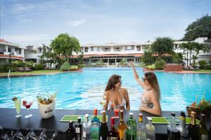 two women sitting at a bar in front of a swimming pool at Heritage Village Resort & Spa Goa in Cansaulim