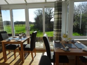 a dining room with two tables and chairs and windows at Hunters Croft in Sway