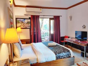 een slaapkamer met een bed, een bureau en een televisie bij The Camelot Beach Resort - Baga in Baga