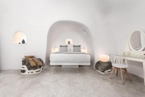 a white bedroom with a bed and a dressing table at Caldera Premium Villas in Oia
