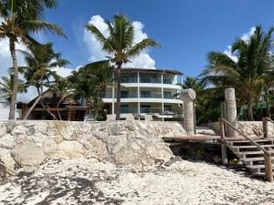 a building on the beach with palm trees in the background at Casa del Puerto by MIJ - Beachfront Hotel in Puerto Morelos