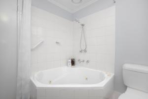 a white bathroom with a tub and a toilet at Glenelg Oasis Studios in Adelaide