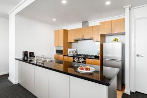 a kitchen with white cabinets and a refrigerator at Quest Southbank in Melbourne