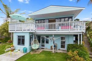 ein blaues Haus mit einem Balkon und einer Terrasse in der Unterkunft Waipu Cove Palm Cottage - Waipu Cove Holiday Home in Waipu