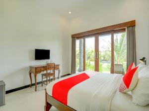 a bedroom with a bed and a desk and a television at OYO 90116 Carik Bali Guest House in Canggu