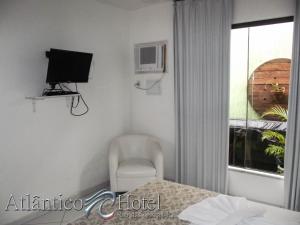 a room with a chair and a tv and a window at Atlântico Hotel in Rio das Ostras