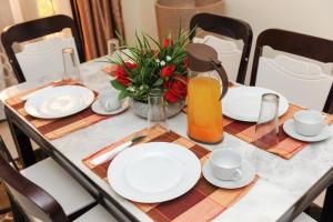 una mesa con platos blancos y una jarra de zumo de naranja en Eric Wilkins Apartments, en Kampala
