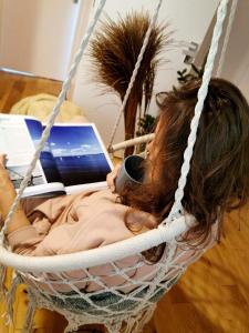 una ragazza sdraiata su un'amaca con un portatile di Relax Houses - Domy Mazur a Małkinie
