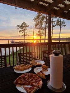 a table with three plates of pizza on it with the sunset at Dances Bay in Elizabeth City