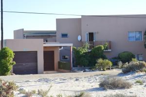 a white house with a garage in the desert at Khoinonia Guesthouse in Port Nolloth