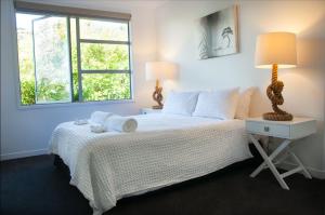 a white bedroom with a bed and a window at The Condo On The Beach - Onetangi - Luxury at The Sands by Waiheke Unlimited in Onetangi