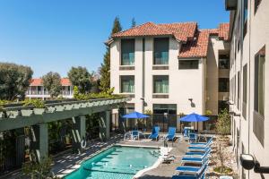 聖克拉拉的住宿－聖克拉拉矽谷快捷假日&套房酒店，一座带椅子和遮阳伞的游泳池位于一座建筑旁边