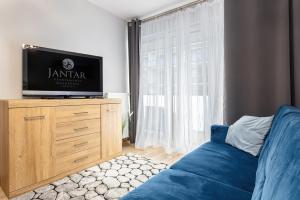 a bedroom with a tv on a dresser with a blue couch at Jantar Apartamenty - Apartamenty KASPROWICZA in Kołobrzeg