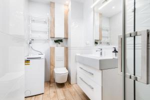 a white bathroom with a sink and a toilet at Jantar Apartamenty - Bałtycka 6 in Kołobrzeg