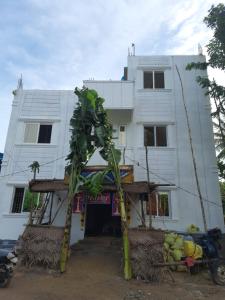 a white building with a palm tree in front of it at Hotel Aishwariyam in Tirukkadaiyūr