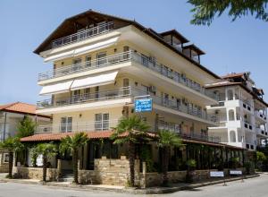 a large white building with palm trees in front of it at Nepheli Apartments and Studios in Paralia Katerinis