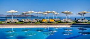 a pool with chairs and umbrellas next to the ocean at Corinna Mare in Kalamaki
