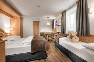 un osito de peluche sentado en una cama en una habitación de hotel en Family Hotel Serena en Andalo