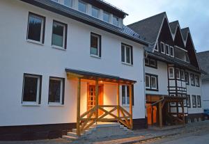 ein weißes Haus mit einer offenen Tür und einer Holzveranda in der Unterkunft Aparthotel Jägerhaus in Willingen