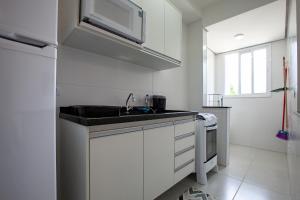una cucina bianca con lavello e microonde di Home Resort Palmeiras II - proximo Praia Grande a Ubatuba