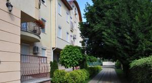 a building with a tree next to a street at Lux Apartmanok in Hajdúszoboszló