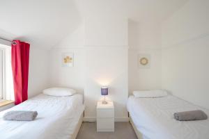 two beds in a room with white walls and red curtains at Avocet House in Wells next the Sea