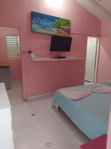 Habitación con cama y TV en una pared rosa. en Hotel Tipico Maura en Bayahibe