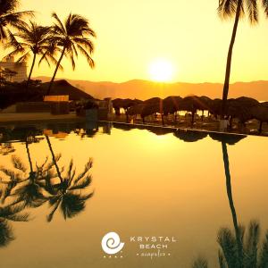 a pool of water with palm trees and the sunset at Krystal Beach Acapulco in Acapulco