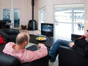 two men sitting on chairs in a living room watching a television at 18 person holiday home in Idestrup in Marielyst