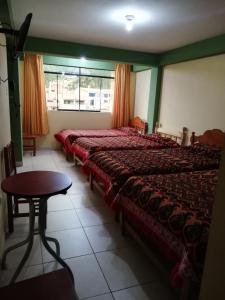 a bedroom with two beds and a table and a window at Artesonraju Hostel Huaraz in Huaraz