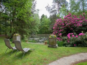 een tuin met 2 stoelen en bloemen en een vijver bij Delightful Chalet in Opglabbeek near Lake in Opglabbeek