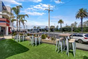 a group of tables and stools on a lawn with a street at The Esplanade Resort And Spa in Lakes Entrance