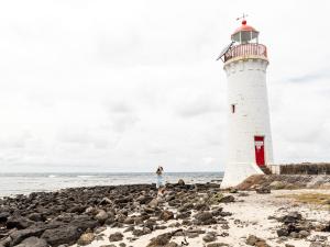 a woman standing next to a lighthouse on a rocky beach at Central Starboard in Port Fairy