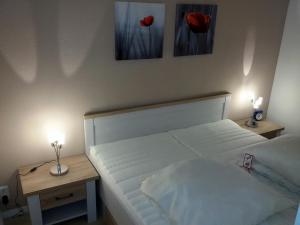 ein weißes Bett mit zwei Tischen und zwei roten Blumen an der Wand in der Unterkunft Ferienpark L10-008 Ferienpark in Heiligenhafen