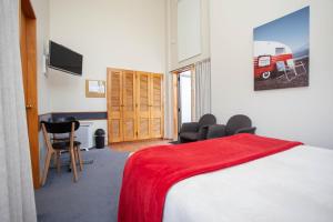 a bedroom with a bed, chair, desk and a television at Cascades Lakefront Motel in Taupo
