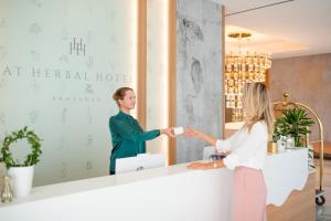 a woman standing in front of a reception desk in front of a mirror at At Herbal Boutique Hotel & Spa in Protaras
