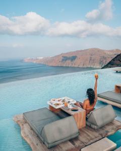 a woman sitting on a table in the middle of the water at Cavo Tagoo Santorini in Imerovigli